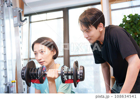 スポーツジムで運動する女性とトレーナー(ダンベル) スポーツジムで運動する女性とトレーナー(ダンベル) 108634541