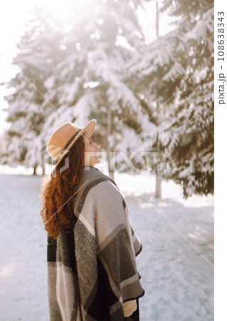 Smiling woman enjoying winter moments in snowy park. Young woman wearing hat, plaid scarf and coat. Smiling woman enjoying winter moments in snowy park. Young woman wearing hat, plaid scarf and coat. 108638343