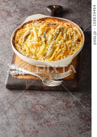 Janssons frestelse casserole consists of potatoes and anchovies which are layered with onions and then doused in cream closeup on the baking dish. Vertical 108639464