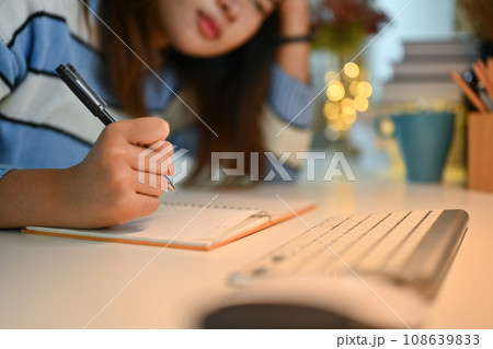 Bored asian woman sitting studying and doing homework a desk in living room Bored asian woman sitting studying and doing homework a desk in living room 108639833