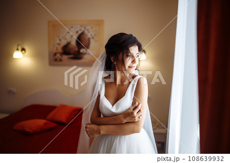 Morning of the bride. Beautiful smiling brunette bride in a white dress with a wedding bouquet in her hands. 108639932
