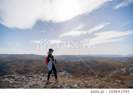 woman on mountain peak looking in beautiful mountain valley in autumn. Landscape with sporty young woman, blu sky in fall. Hiking. Nature woman on mountain peak looking in beautiful mountain valley in autumn. Landscape with sporty young woman, blu sky in fall. Hiking. Nature 108641995