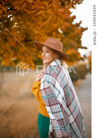 autumn woman in a green dress, brown hat, plaid, against the background of an autumn tree autumn woman in a green dress, brown hat, plaid, against the background of an autumn tree 108642004