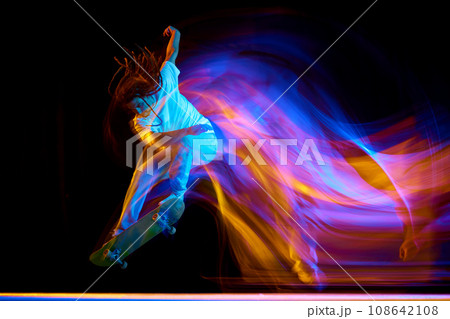 Man skateboarder performing freestyle tricks in motion isolated black background in mixed neon flashes of light. Concept of youth culture. Man skateboarder performing freestyle tricks in motion isolated black background in mixed neon flashes of light. Concept of youth culture. 108642108