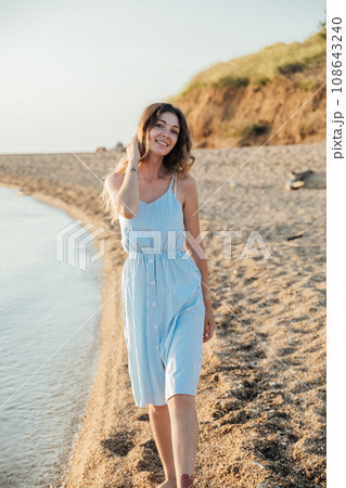 a woman in a sundress walks along the seashore on the beach walk 108643240