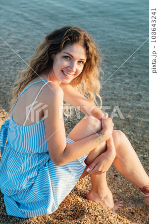 a woman in a sundress sitting by the sea on the beach rest 108643241