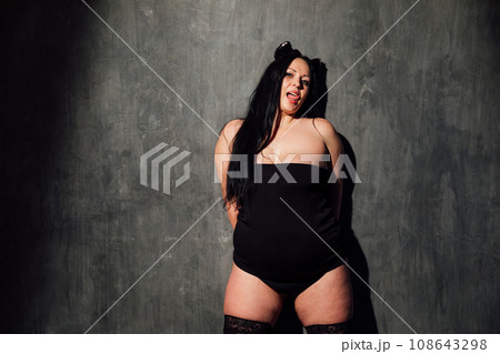 a fat woman in stockings stands on a black background 108643298