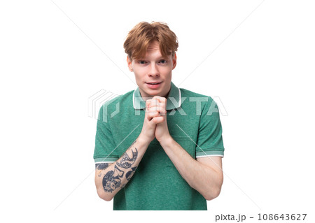 young handsome red-haired man dressed in a green t-shirt looks at the camera on the background with 108643627