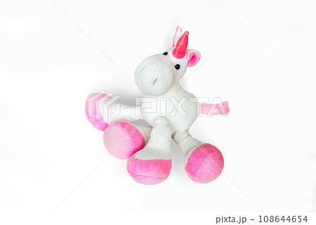 Pink soft unicorn toy sitting at white background. Isolated studio image 108644654
