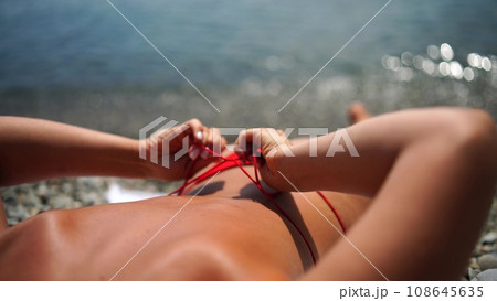 Woman taking red bikini off on beach for tan, lady stripping holiday swimsuit with bow in string. Fun and relax, sexy model untying swimming costume bra, happy woman in swimwear on vacation Woman taking red bikini off on beach for tan, lady stripping holiday swimsuit with bow in string. Fun and relax, sexy model untying swimming costume bra, happy woman in swimwear on vacation 108645635