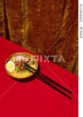 Asian culture, cuisine. Popular recipes. Plate with noodles, egg and meet, served with greenery isolated red background. Asian culture, cuisine. Popular recipes. Plate with noodles, egg and meet, served with greenery isolated red background. 108646316