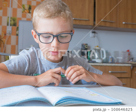Tired sad little child boy sits at a table in the kitchen and writes homework. Boring lessons. 108646825