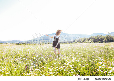 a woman in a straw hat walks in a field with daisies flowers in nature 108646956