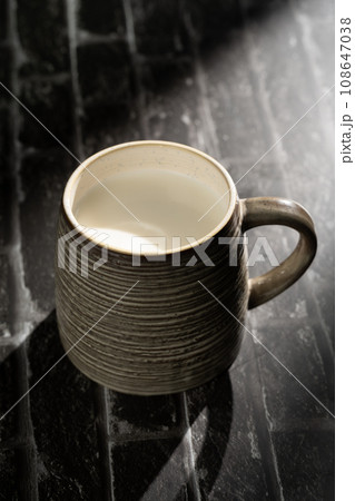 Sunlight shining on a slate board with a cup of milk. 108647038