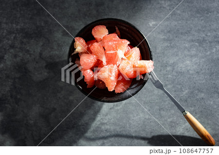 Sunlight shining on grapefruits with red flesh placed on a slate board in a bowl. 108647757