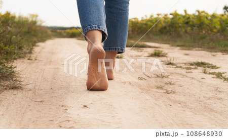 Woman walking in field meadow. Close-up of bare feet soiled with the ground. Woman walking in field meadow. Close-up of bare feet soiled with the ground. 108648930