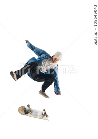 Dynamic image of sportive young man in casual clothes in motion, raining, jumping with skateboard isolated over white background 108649043