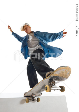 Dynamic image of teen boy in blue shirt and capo training, in motion, skateboarding isolated over white background Dynamic image of teen boy in blue shirt and capo training, in motion, skateboarding isolated over white background 108649053