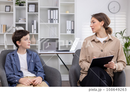 A pediatric psychologist consults a teenage boy, working inside a medical consulting room. 108649263