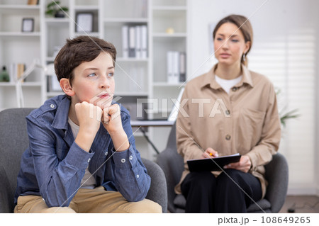 A pediatric psychologist consults a teenage boy, working inside a medical consulting room. 108649265