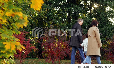 Family with boy in warm coats walks through botanical garden holding hands at warm daylight. Family leads little boy along path spending time together. Family enjoys last warm autumn days in park Family with boy in warm coats walks through botanical garden holding hands at warm daylight. Family leads little boy along path spending time together. Family enjoys last warm autumn days in park 108651672