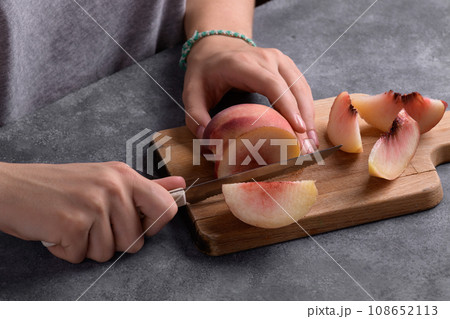 Authentic female hands cutting a fresh ripe peach on wooden cutting board, food lifestyle Authentic female hands cutting a fresh ripe peach on wooden cutting board, food lifestyle 108652113