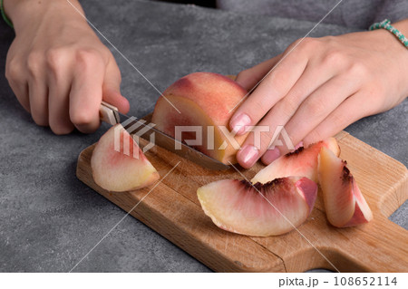Authentic female hands cutting a fresh ripe peach on wooden cutting board, food lifestyle Authentic female hands cutting a fresh ripe peach on wooden cutting board, food lifestyle 108652114