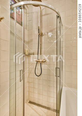 a bathroom with a glass shower door and tiled walls in the corner to the left is a white bathtub on the right side a bathroom with a glass shower door and tiled walls in the corner to the left is a white bathtub on the right side 108654219