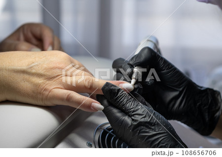 Manicurist at work. Professional manicurist removes old worn nail design from nails of client using modern electric drill. Preparing fingernails for making fresh manicure and applying new nail design 108656706