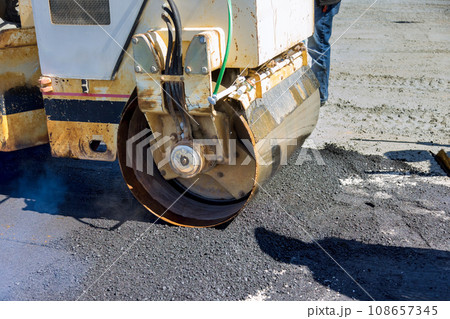 As asphalt is being laid on new road worker uses an asphalt roller compactor 108657345