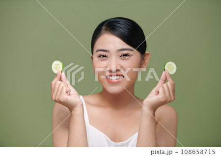 Young beautiful asian lady holding slices of cucumber near her face and smiling 108658715