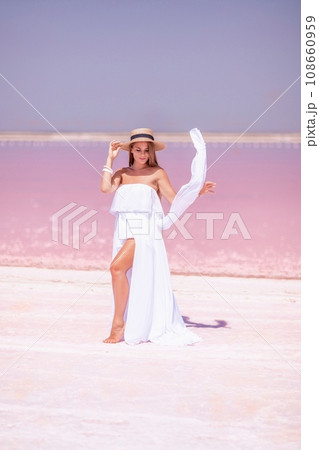 Woman in pink salt lake. She in a white dress and hat enjoys the scenic view of a pink salt lake as she walks along the white, salty shore, creating a lasting memory. Woman in pink salt lake. She in a white dress and hat enjoys the scenic view of a pink salt lake as she walks along the white, salty shore, creating a lasting memory. 108660959