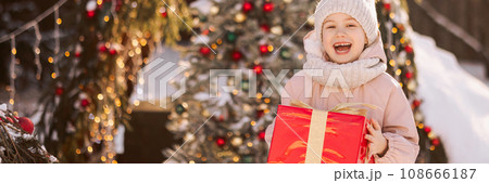Banner little girl with a Christmas gift outdoors in winter on Christmas Eve. 108666187