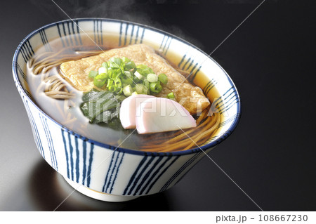 油揚げ、かまぼこ、ワカメ、葱が乗った熱々きつね蕎麦を黒背景で撮影 108667230