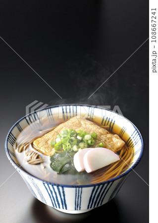油揚げ、かまぼこ、ワカメ、葱が乗った熱々きつね蕎麦を黒背景で撮影 108667241