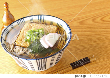 油揚げ、かまぼこ、ワカメ、葱が乗った熱々きつね蕎麦と瓢箪型の唐辛子入れ 108667470