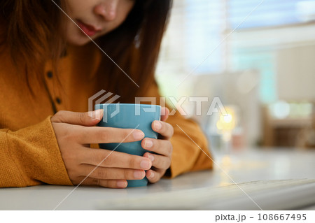 Close up young woman with cup of herbal tea relaxing in morning at cozy home Close up young woman with cup of herbal tea relaxing in morning at cozy home 108667495