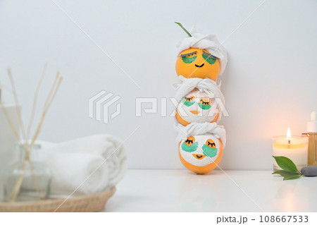 Three orange fruits in face mask near candle on white table. Spa treatment and self care concept 108667533