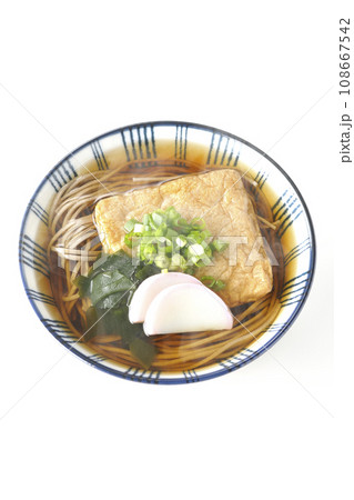 油揚げ、かまぼこ、ワカメ、葱が乗った熱々のきつね蕎麦を白背景で俯瞰撮影 108667542