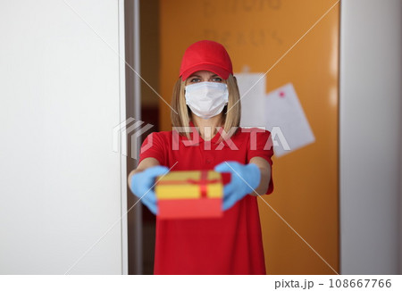Woman courier in protective medical mask and gloves giving gift 108667766