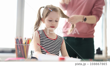 Little girl drawing with pencils. Mother braiding child hair 108667865