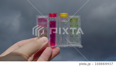 Water samples for PH and chlorine levels. Hand holding against the sky - checking the quality of water in the pool Water samples for PH and chlorine levels. Hand holding against the sky - checking the quality of water in the pool 108669437
