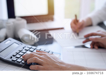 Two accountants use a calculator and laptop computer for counting taxes or revenue balance. Business, audit, and taxes concepts 108674718
