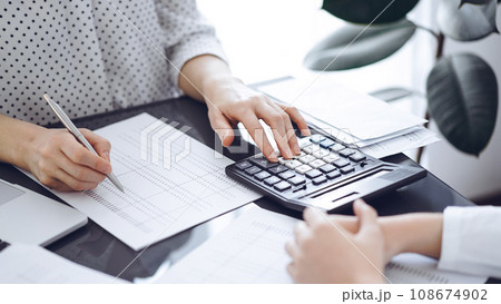 Woman accountant using a calculator and laptop computer while counting taxes with a client or a colleague. Business audit team, finance advisor Woman accountant using a calculator and laptop computer while counting taxes with a client or a colleague. Business audit team, finance advisor 108674902