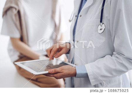 Doctor and patient in clinic. Friendly physician using tablet computer near a young woman. Medicine concept 108675025