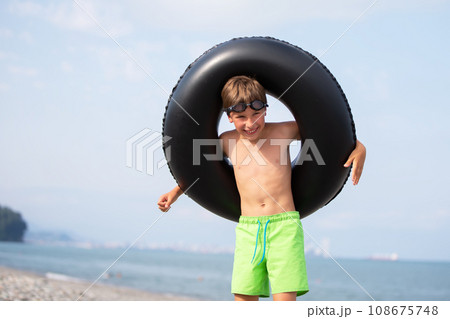 Happy boy with swimming ring and goggles by the sea. 108675748