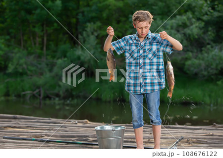A fisherman boy admires his catch. Fishing child. 108676122
