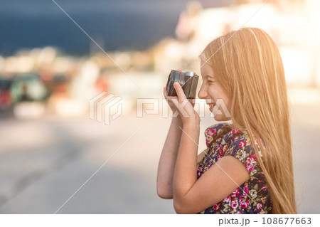 Beautiful little girl with camera takes a picture, summer outdoor 108677663