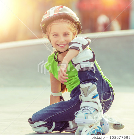 Cute little girl on roller skates in helmet at a park Cute little girl on roller skates in helmet at a park 108677693