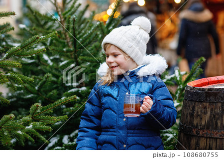 Little cute preschool girl drinking hot children punch or chocolate on German Christmas market. Happy child on traditional family market in Germany, Laughing boy in colorful winter clothes 108680755